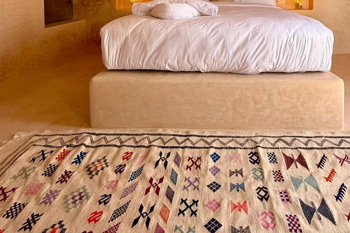 Une chambre à coucher avec un lit, deux lampes de chevet, un plaid à motifs et un mur à texture.
