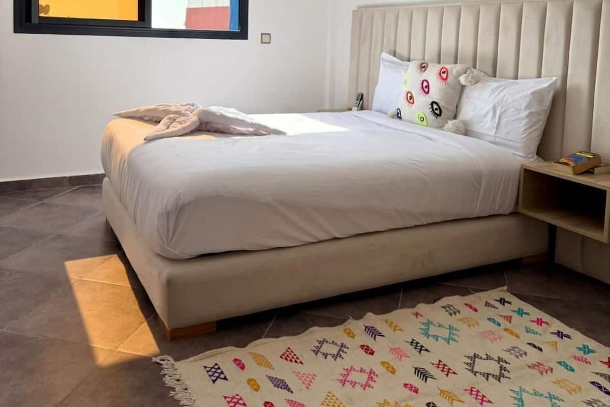 Une chambre moderne avec un grand lit, une fenêtre offrant une belle vue, un élément décoratif mural et un tapis à motifs.