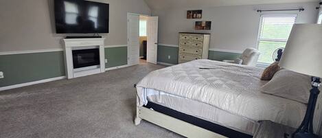 A bedroom with a bed, a ceiling fan, a TV, a dresser, and a window with blinds.