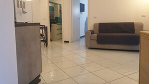Una sala de estar con sofá, una mesa de comedor con sillas y una cocina visible a través de un vano abierto.