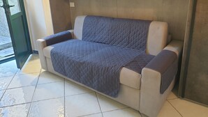 Un sofá beige con funda acolchada azul, ubicado frente a una pared con estantería empotrada.