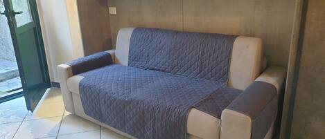 Un sofá beige con funda acolchada azul, ubicado frente a una pared con estantería empotrada.