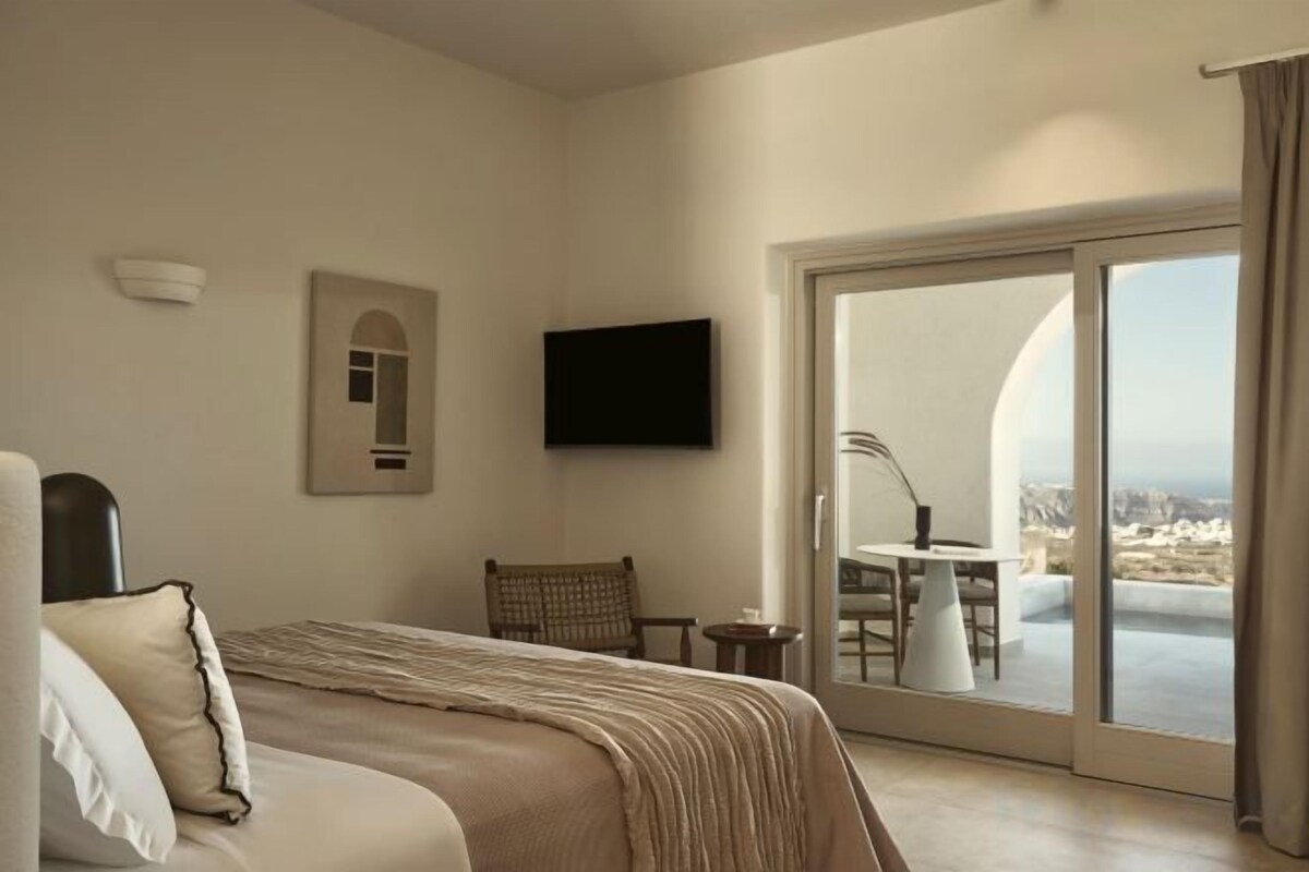 A hotel room with a bed, a television, a chair, a small table, and a view through a sliding door.