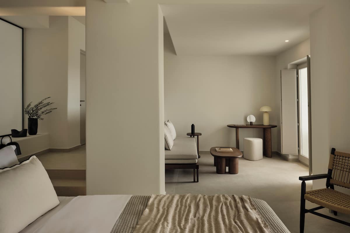 Quarto de hotel moderno com uma cama, uma cadeira, uma mesinha e um espelho.