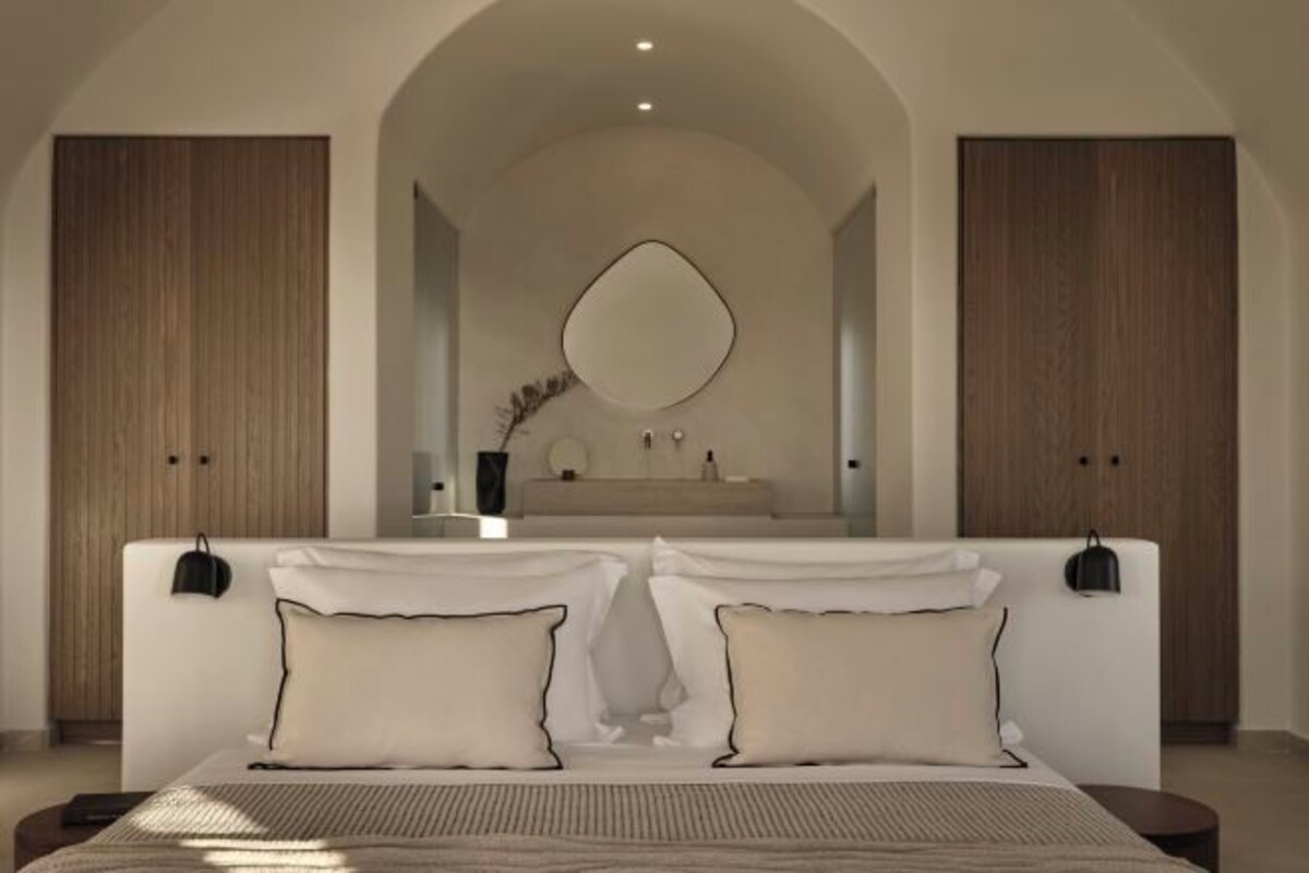 A bedroom with a large bed, a mirror above the dresser, and wooden wardrobes.
