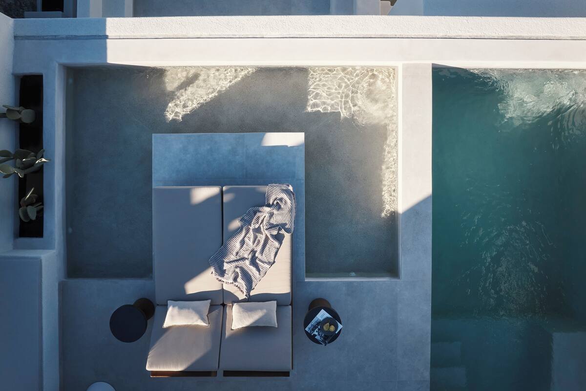 Vista aérea de uma área de piscina moderna, com espreguiçadeira, duas almofadas e uma revista no chão.