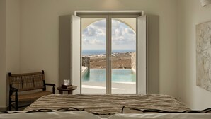 Une chambre avec un grand lit, une chaise, une petite table avec un verre, et une vue sur une piscine et un paysage.