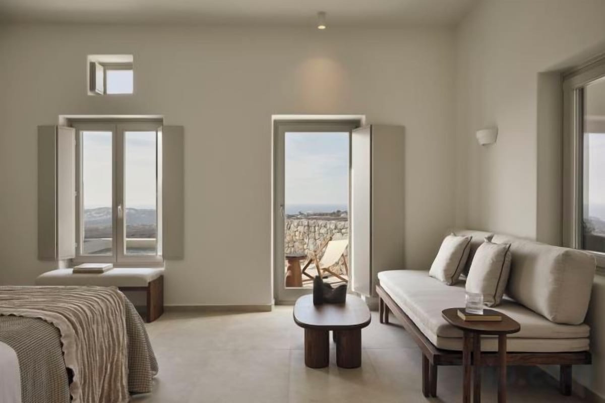 Una habitación con cama, sofá, una mesita y ventanas amplias que ofrecen vistas.