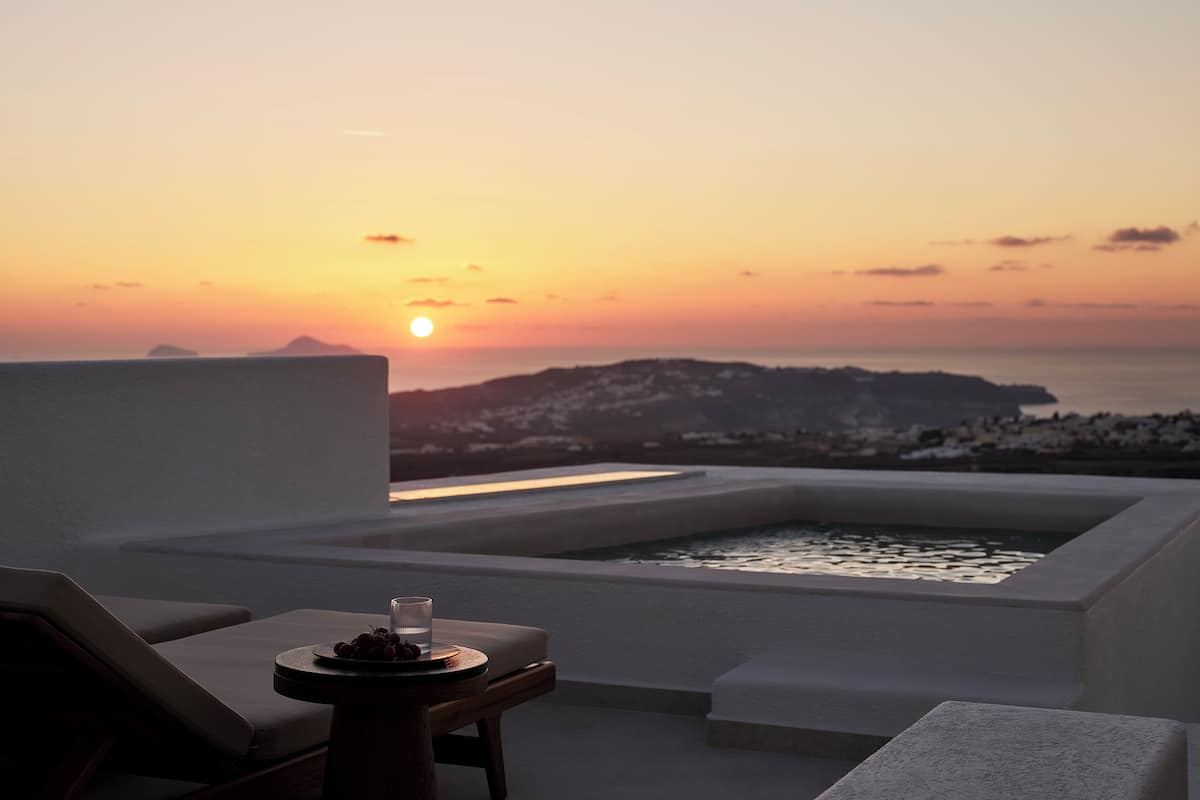 Vista do pôr do sol a partir de um terraço no telhado, com hidromassagem, espreguiçadeiras e uma mesa com uma taça e uvas.