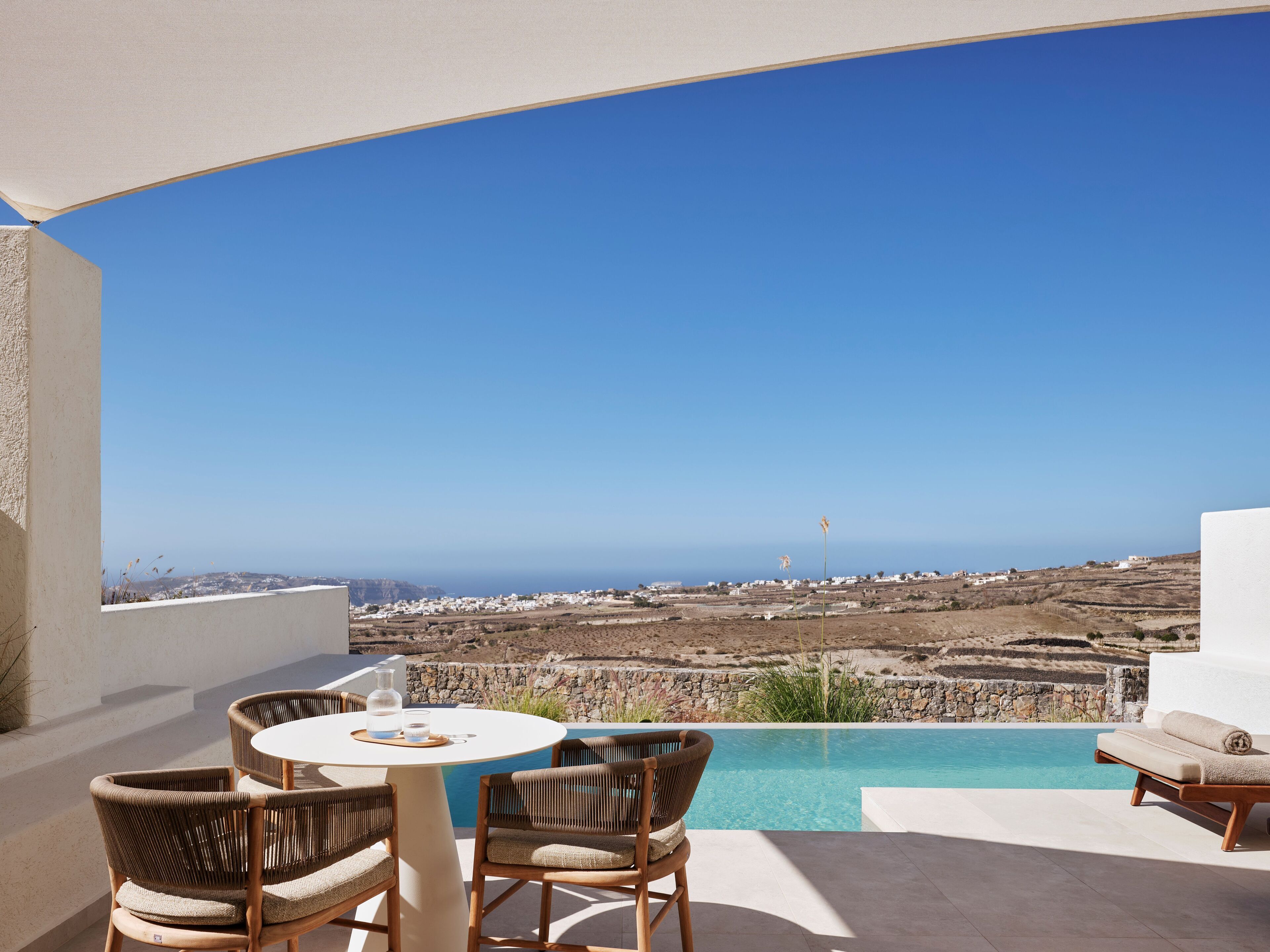 A terrace with a pool, wicker chairs, and a table with a bottle and glasses.