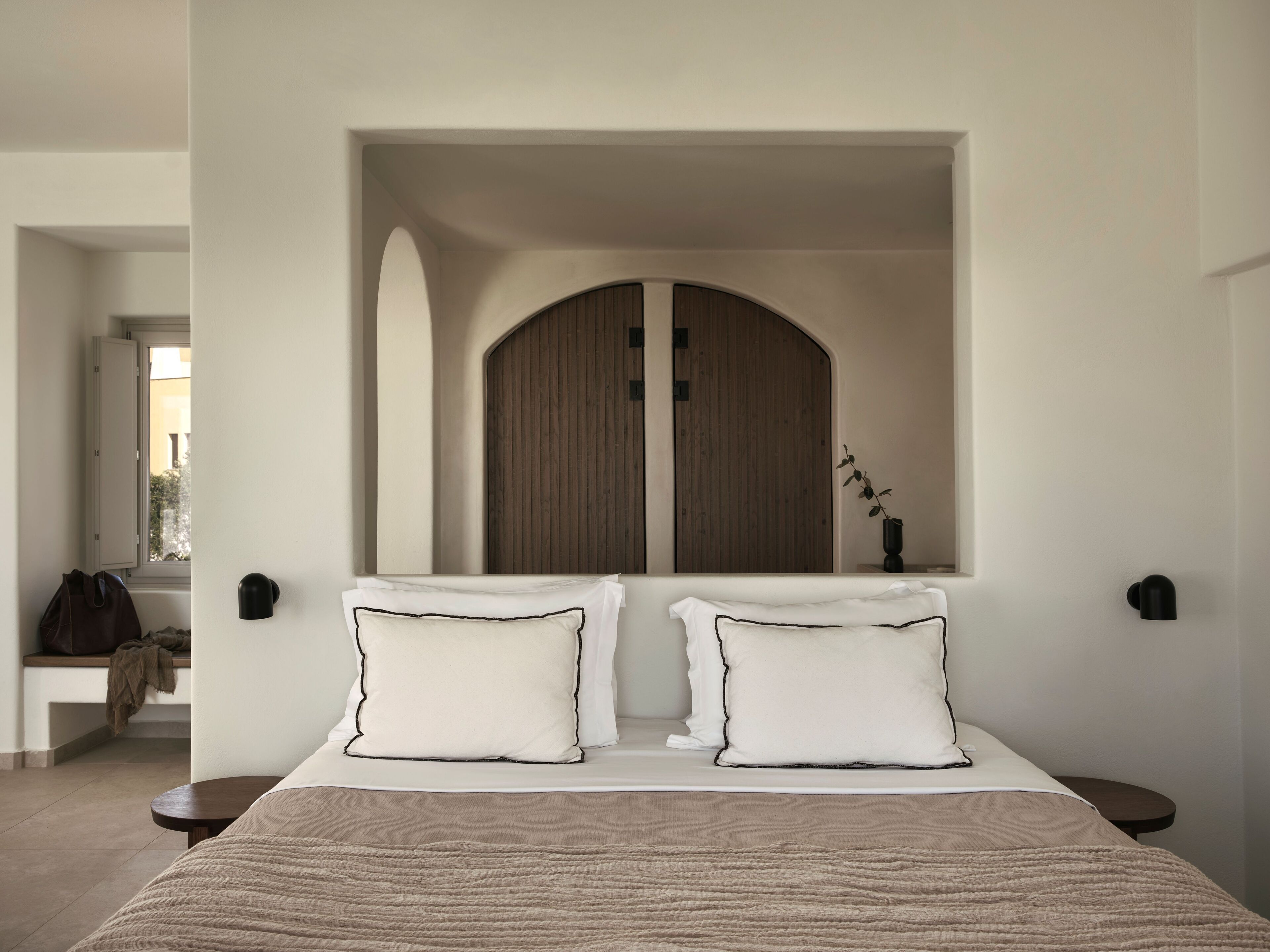 Habitación de hotel con una cama grande, dos mesitas de noche, una puerta de madera y vistas al exterior.