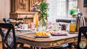 Ett matbord i trä med en blomsterdekoration i mitten, olika sorters frukostmat och köksredskap i vintage-stil.