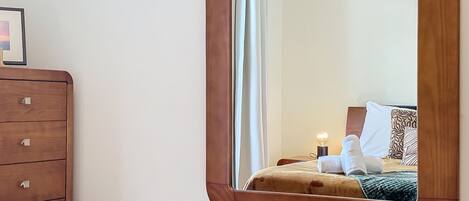 A bedroom with a wooden dresser, a large mirror, and a bedside table.
