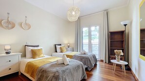 Una camera d'albergo con due letti, un comodino con una lampada, un tavolino con un vaso e una libreria.