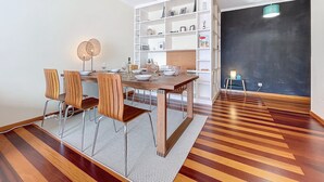 Zona pranzo con tavolo e sedie in legno, una libreria bianca e una parete con lavagna.