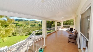 A covered balcony with a view of a green landscape, a patio area with a table and chairs, and a green watering can. - Casa Bianca (A dos Francos)