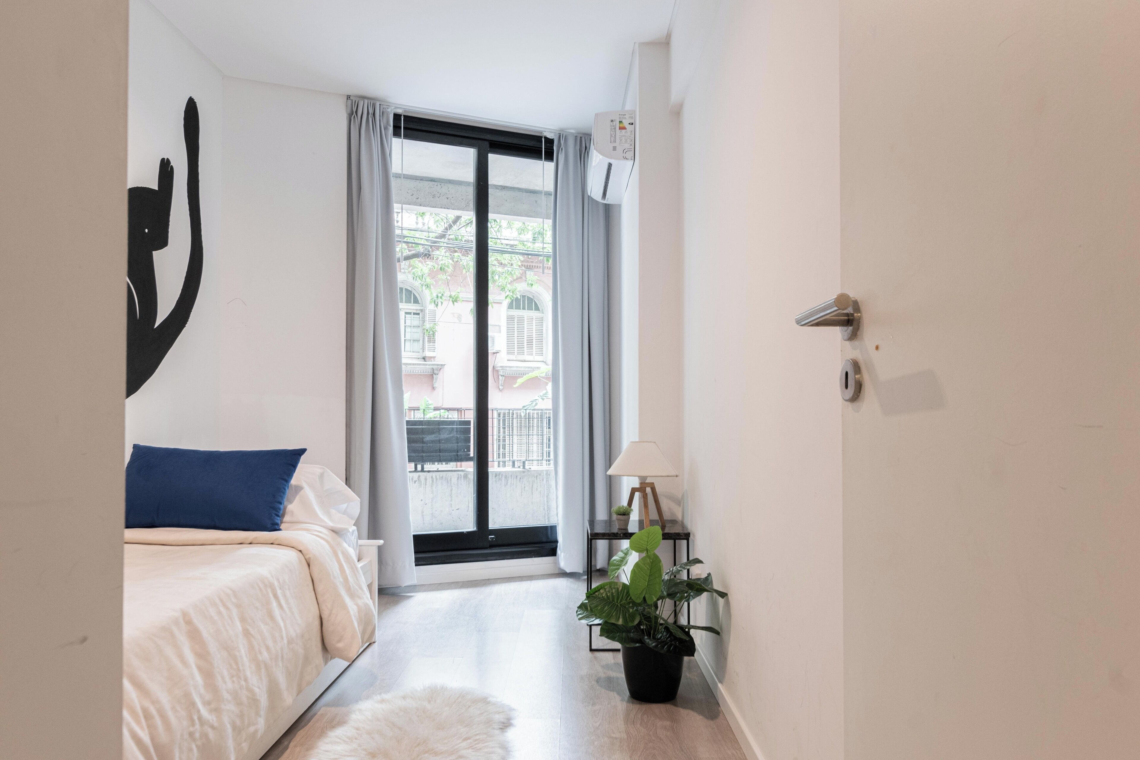 Een slaapkamer met een bed, een kamerplant, een lamp en uitzicht.