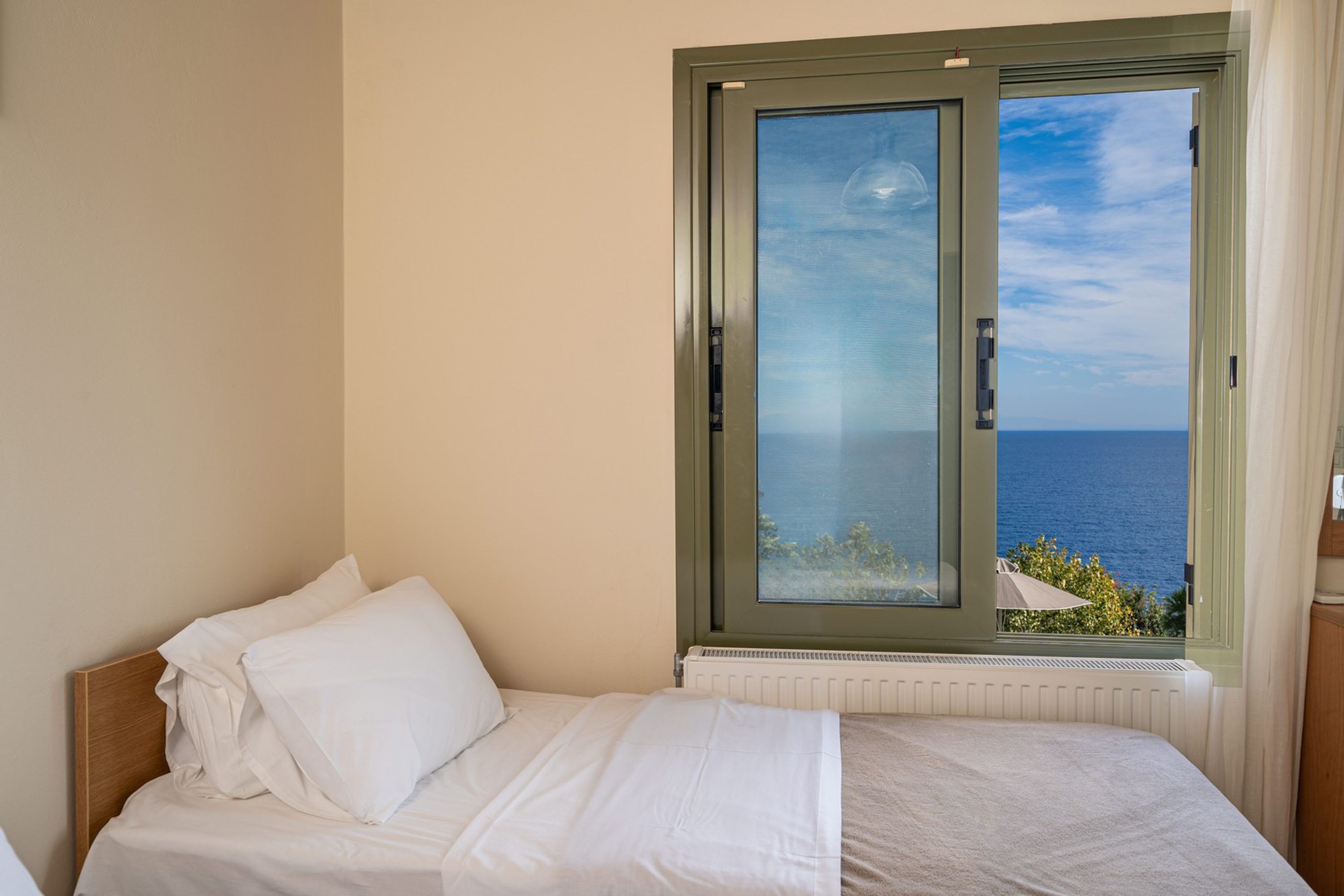 Una cama individual con ropa de cama blanca en una habitación con vistas al mar a través de un ventanal.