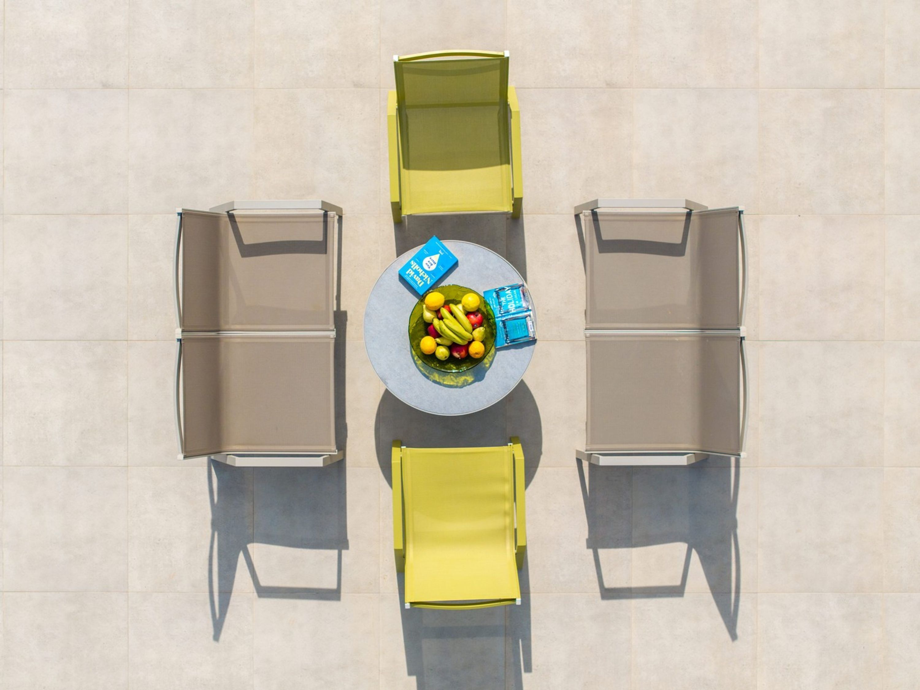 Vue plongeante d’un coin repas avec une table ronde, quatre chaises et un saladier rempli de fruits.