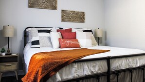 Un letto rifatto con cura, con diversi cuscini e una coperta marrone. Sopra il letto, due elementi decorativi fissati alla parete.