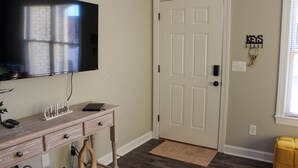 Una stanza con una TV a schermo piatto fissata al muro, una scrivania in legno con cassetti, una porta bianca e un piccolo tappeto sul pavimento.