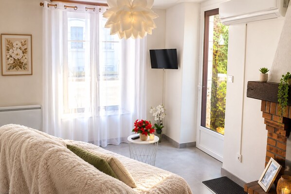 A cozy room with a sofa, a flat-screen TV, a fireplace, and a window with curtains. - Apartment for 4 People in the Heart of the Medieval City (Mennetou-sur-Cher)