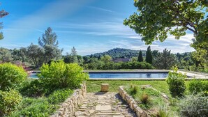 Ein Steinweg führt zu einem Pool, der von üppigem Grün und Bäumen umgeben ist.