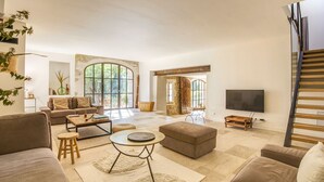 Ein geräumiges Wohnzimmer mit großem Fenster, einer Couch, einem Couchtisch und einem Fernseher.