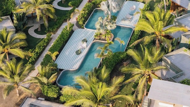 An aerial view of a resort with multiple swimming pools surrounded by palm trees and lush greenery. - Samas Hotel - La Saladita (Saladita)