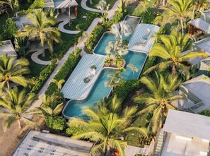 Oversigtsbillede af et resort med flere swimmingpools omgivet af palmer og frodig vegetation.