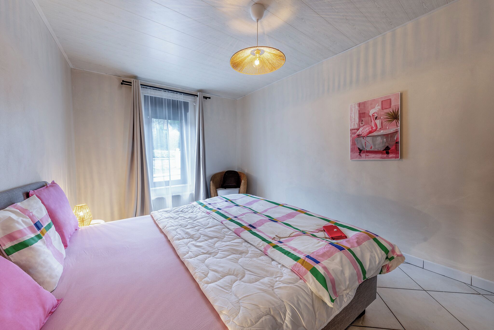 Quarto com cama, cadeira, quadro e luminária no teto.