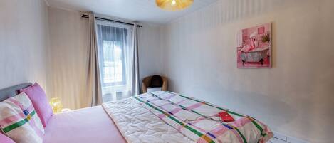 A bedroom with a bed, a chair, a painting, and a ceiling light.