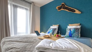 Een net opgemaakt bed met een laptop, een dienblad met eten en drinken, en decoratieve kussens.