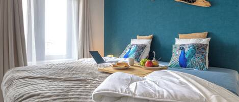A neatly made bed with a laptop, a tray with food and drinks, and decorative pillows.