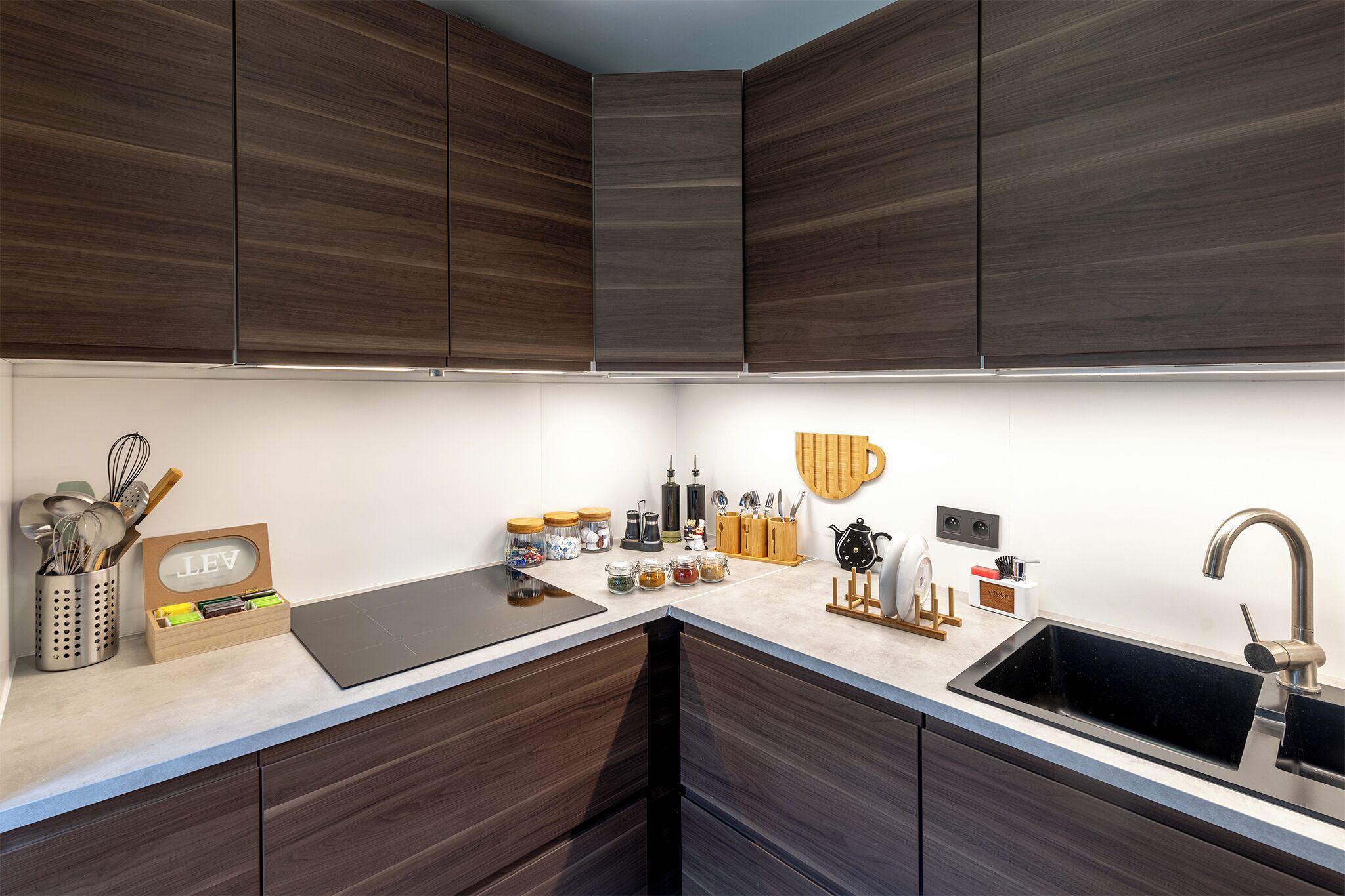 A modern kitchen with dark wood cabinets, a black countertop, and a stainless steel sink.