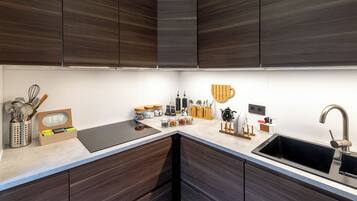 A modern kitchen with dark wood cabinets, a black countertop, and a stainless steel sink.