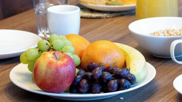 A breakfast table with plates of fruit, waffles, toast, and a glass of orange juice.