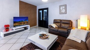 Een moderne woonkamer met een flatscreen televisie, een leren bank, een witte salontafel en een groot raam.