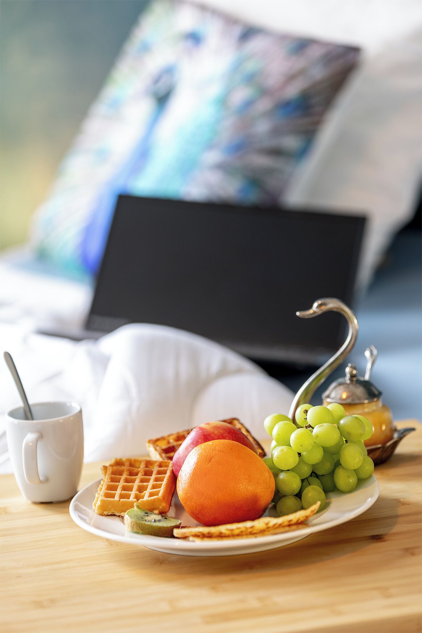 A breakfast setting with waffles, fruit, and a teapot on a table.