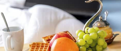 A breakfast setting with waffles, fruit, and a teapot on a table.