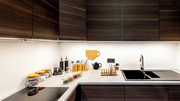 Een moderne keuken met donkerhouten kastjes, een roestvrijstalen spoelbak en een wit aanrecht.