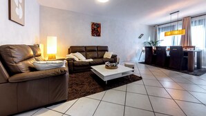 Een moderne woonkamer met een bruine leren bank, een witte salontafel en een eethoek met een houten tafel en stoelen.