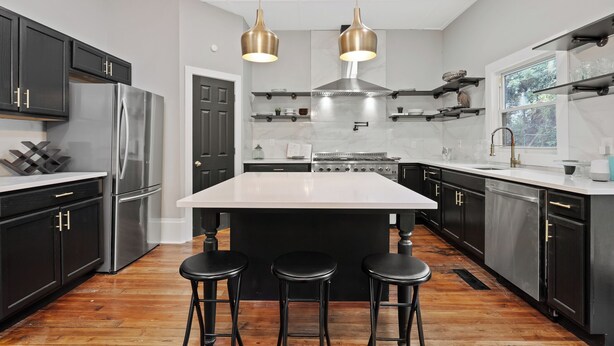 A modern kitchen with black cabinets, stainless steel appliances, a large island with stools, and pendant lighting. - Midnight Sanctuary at Mystic Falls - 3 Bed 2.5 BA Home 1 mi to Covington Square (Covington)