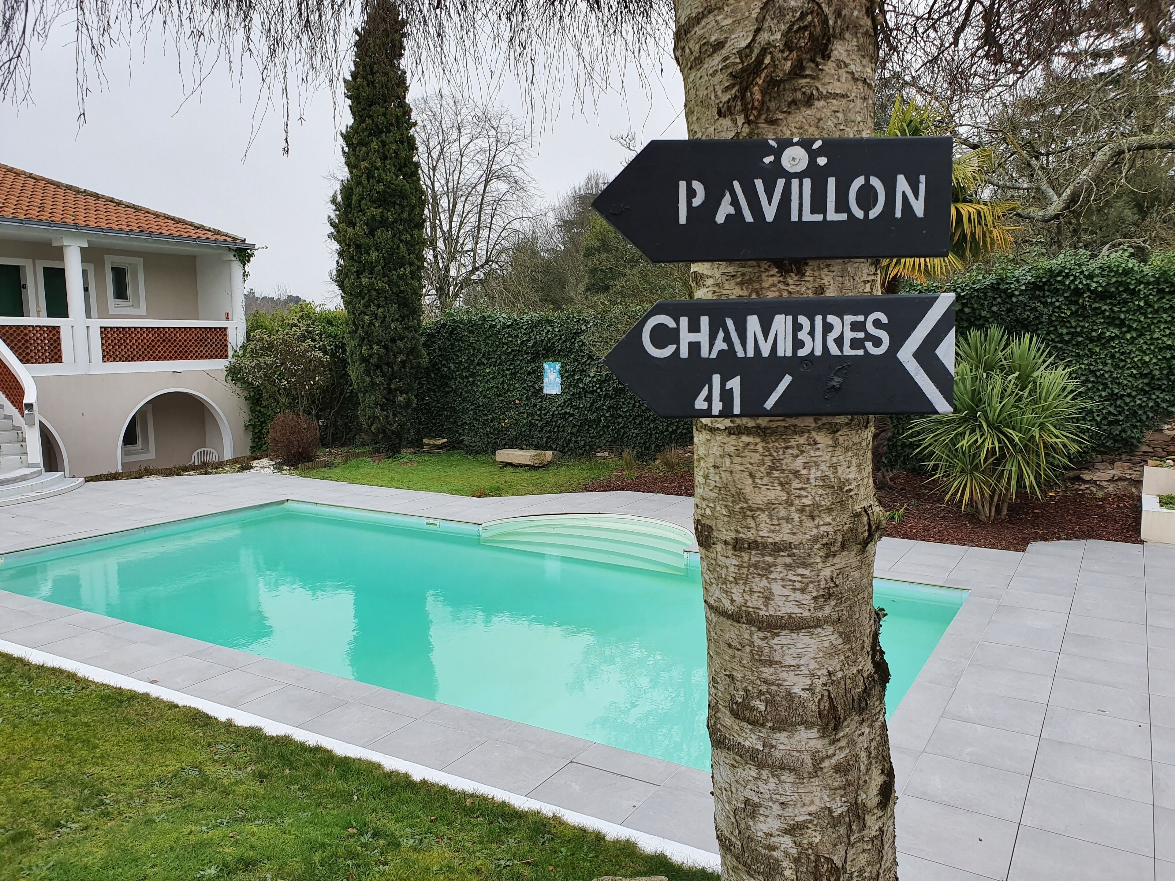 A swimming pool with directional signs for 'Pavillon' and 'Chambres'.
