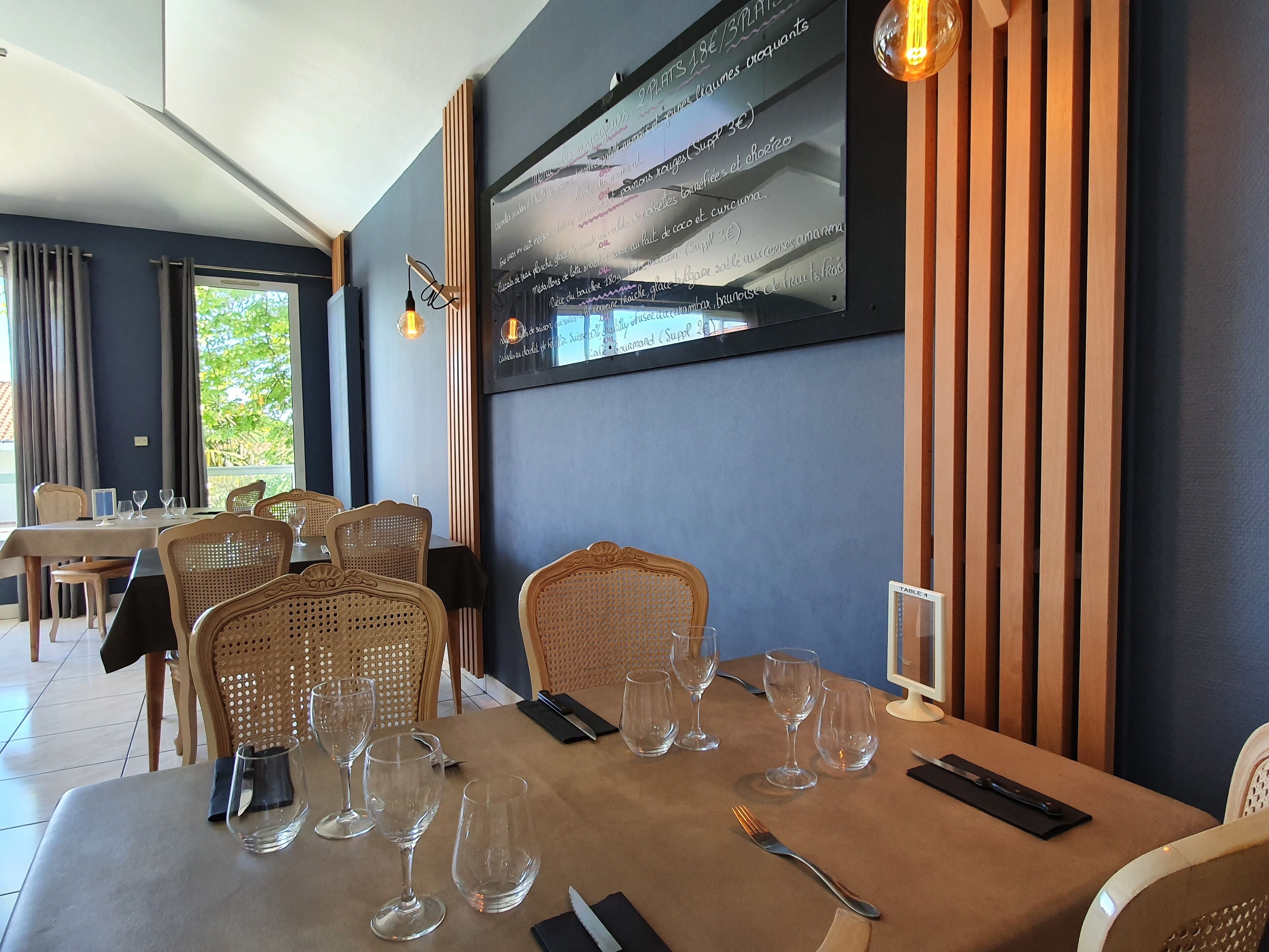A restaurant with a table set for six, including wine glasses, cutlery, and a menu board on the wall.