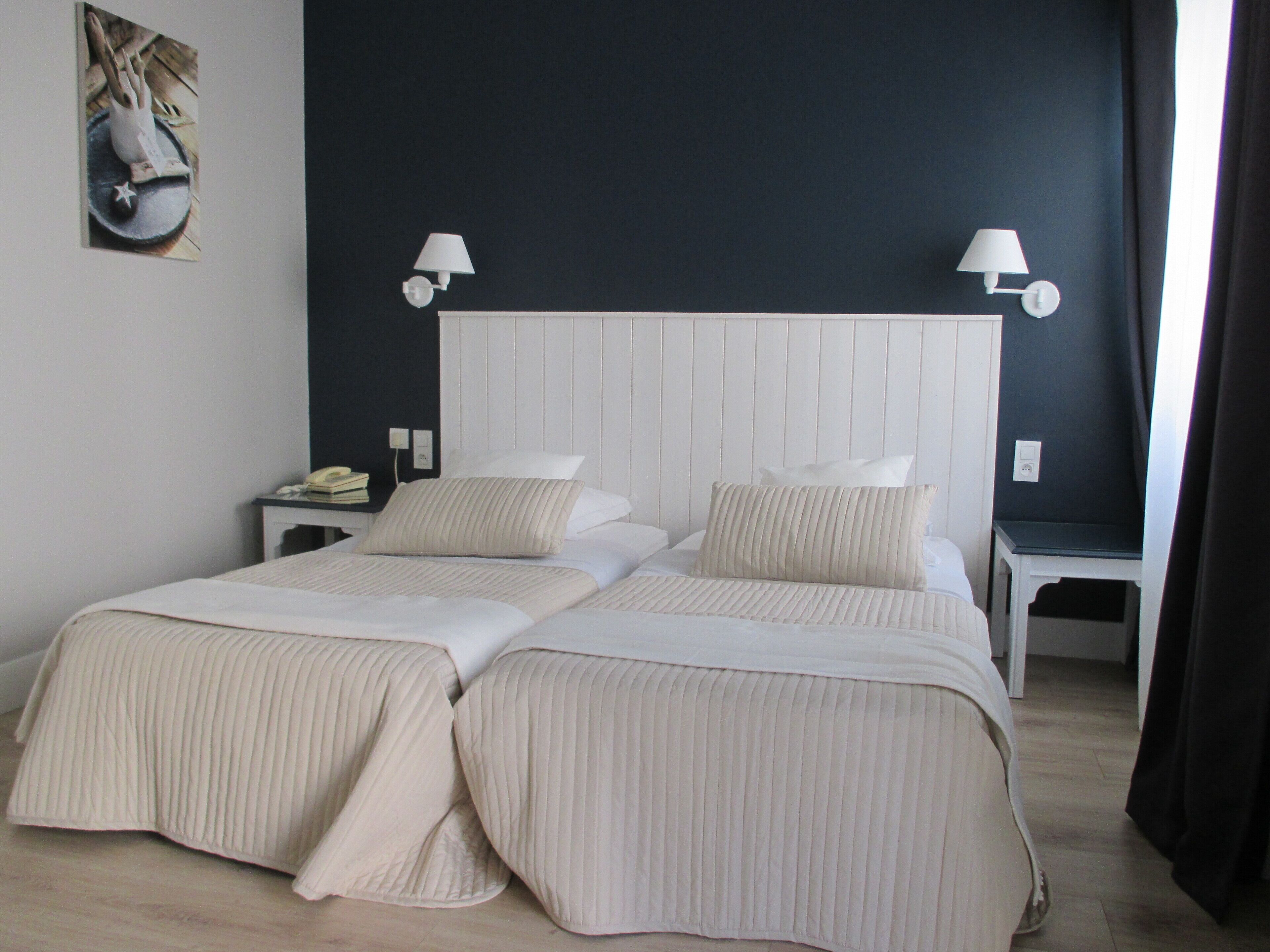 Een tweepersoonsbed met twee kussens, een nachtkastje met een lamp en een kunstwerk aan de muur.