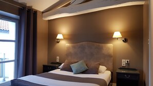 A hotel room with a large bed, two bedside tables, two wall-mounted lamps, and a window with curtains.