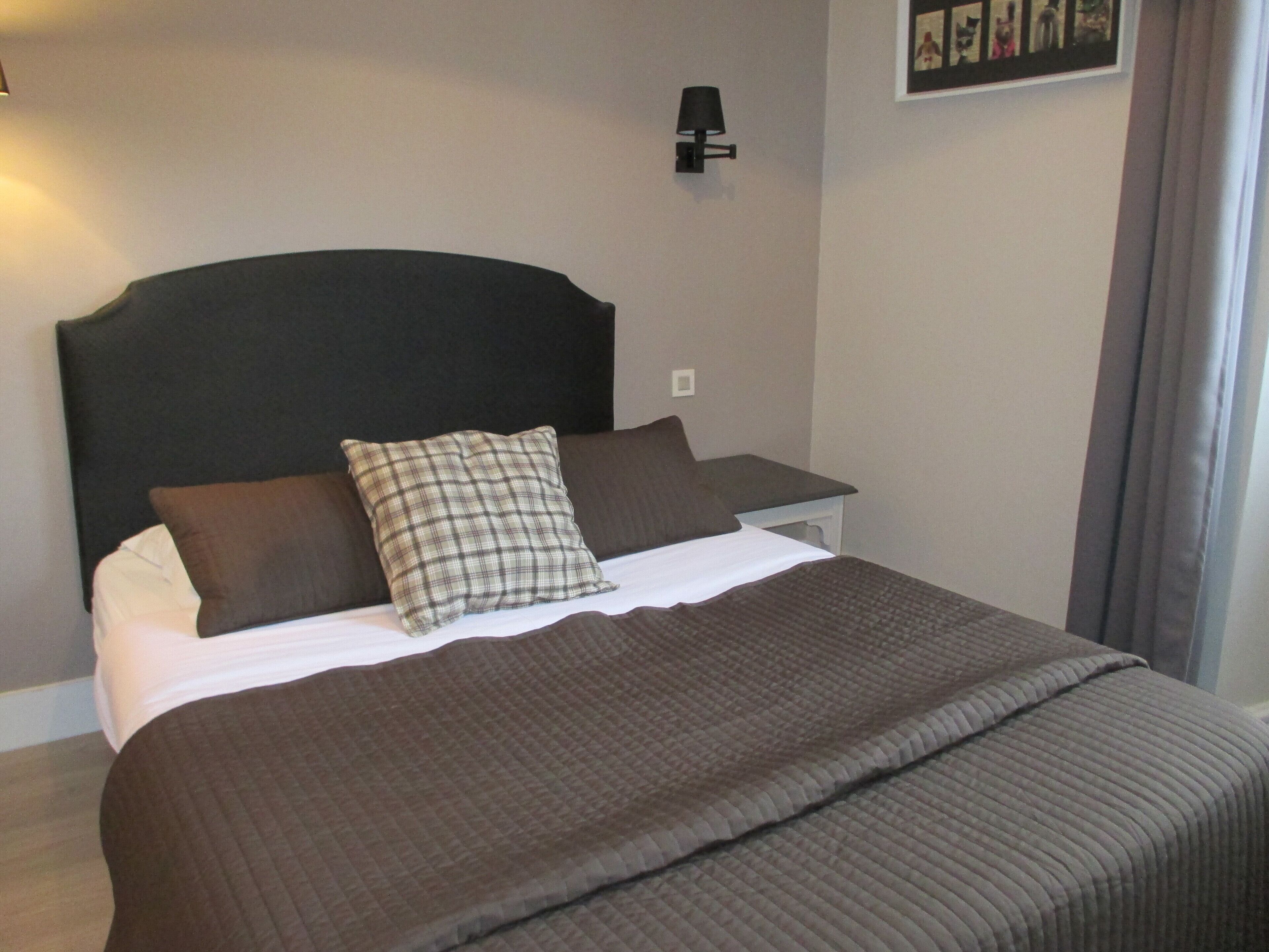 A neatly made bed with a brown quilt, a black headboard, and two pillows, one plaid and one solid brown.