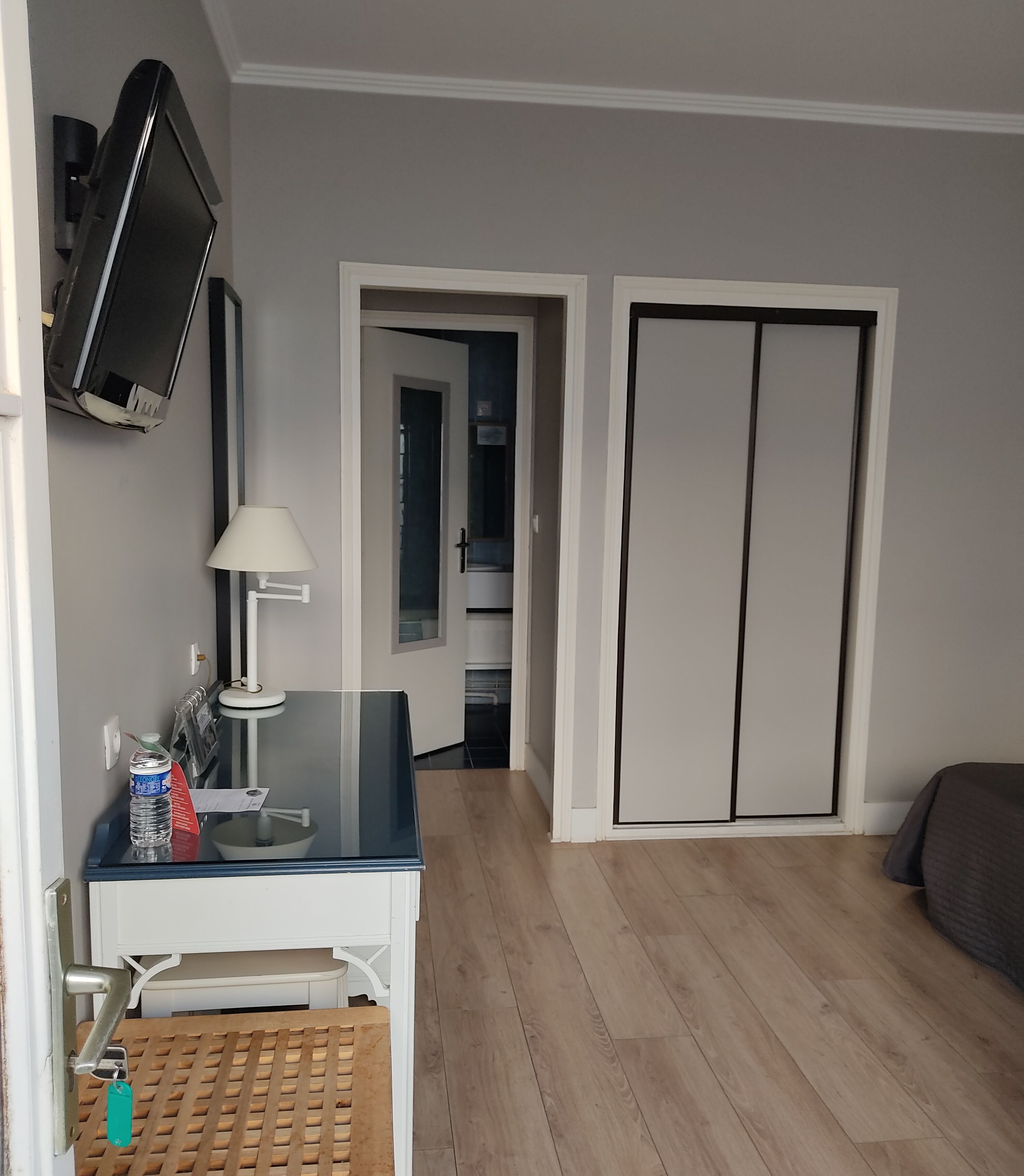 Une chambre comprenant un lit, un bureau avec une lampe, un téléviseur fixé au mur et une armoire.