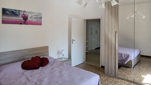 Un dormitorio con cama, mesita de noche, espejo y un cuadro en la pared.